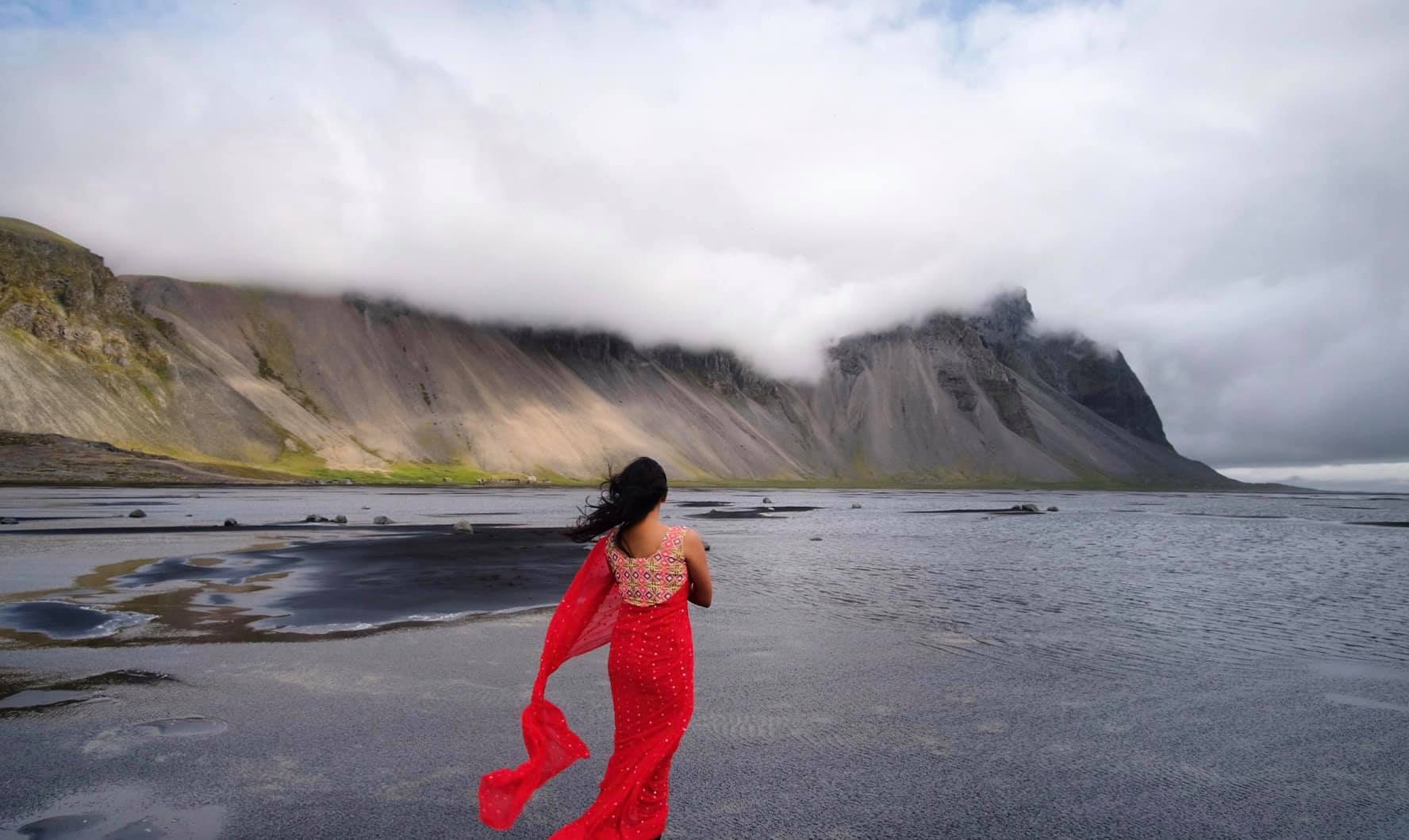 Maitraye is wearing a red saree and admiring the beauty of the Vestrahorn mountain in Iceland